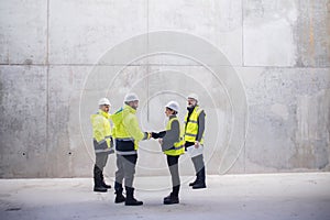 Group of engineers standing on construction site, shaking hands.
