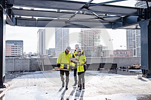 Group of engineers standing outdoors on construction site, using tablet.