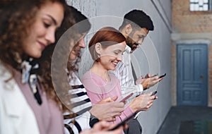 Group of entrepreneurs standing against concrete wall indoors in office, using smartphone.