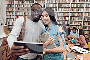 Group of ethnic multicultural students in library. Black guy and asial girl are using tablet.