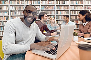 Group of ethnic multicultural students in library. Black guy on laptop.