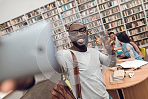 Group of ethnic multicultural students in library. Black guy taking selfie on phone.