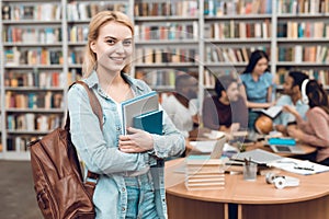 Group of ethnic multicultural students in library. White girl with notebooks.