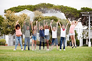 Group Of Excited Elementary School Pupils Standing On Playing Field At Break Time With Arms Raised