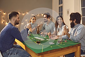 Group of excited friends with playing cards in hands sitting, betting and playing poker