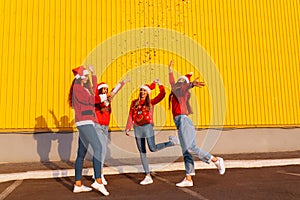 Group of excited happy friends in santa claus hats having fun and jumping with colorful confetti outdoors. New Year celebration