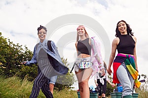 Group Of Excited Young Female Friends Carrying Camping Equipment Through Field To Music Festival