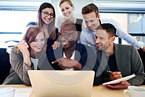 Group of executives smiling gathered around laptop