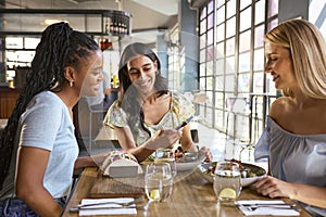Group Of Female Friends Meeting Up In Restaurant Or Coffee Shop Looking At Mobile Phone
