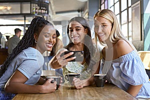 Group Of Female Friends Meeting Up In Restaurant Or Coffee Shop Posing For Selfie On Mobile Phone