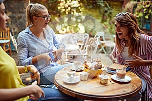 Group of female friends talking in outdoor cafe, showing on their bellies, laughing