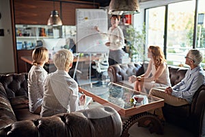 Group of female office staff are sitting on the sofa at workplace and watching their female colleague presentation. Business,