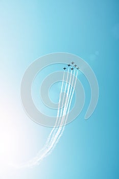 Group of fighter jets flying against a bright blue sky, performing figures from the smoke