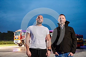 Group of firefighters, dressed in civilian clothing, stand in front of fire trucks during the night, showcasing a moment