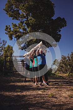 Group of fit women carrying a heavy wooden log during obstacle course training