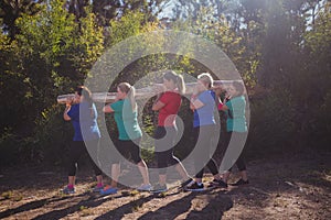 Group of fit women carrying a heavy wooden log during obstacle course training