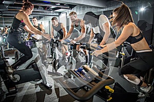 Group of fitness people doing cardio workout on indoor cycling bikes at gym.