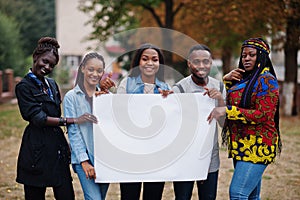 Group of five african college students on campus at university yard hold empty white blank. Free space for your text. Black afro