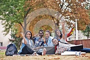 Group of five african college students spending time together on campus at university yard. Black afro friends sitting on grass