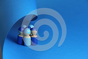 Group of five blue wooden toy people are covered with a blue sheet of paper, blue background with copy space