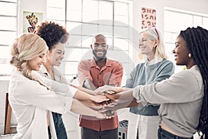 Group of five cheerful diverse businesspeople piling their hands together in an office at work. Happy business