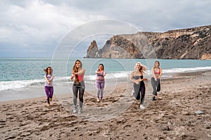 A group of five female friends are doing exercises on the beach. Beach holiday concept, healthy lifestyle