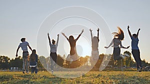Group of five happy friends jumps at sunset time on background mountains.