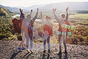 Group of five happy friends jumps at sunset time on background mountains