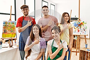 Group of five hispanic artists at art studio cheerful with a smile of face pointing with hand and finger up to the side with happy