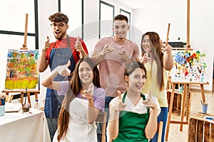 Group of five hispanic artists at art studio pointing fingers to camera with happy and funny face