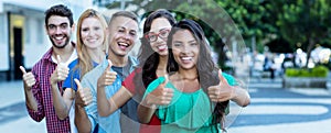 Group of five laughing international young adults in line showing thumbs up