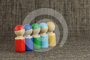 Group of five multicolored wooden toy people are lined up in a diagonal, cloth or fabric background with copy space