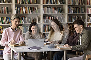 Group of five pupils study together in library use laptop