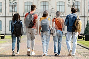 Group of five students with backpacks walking at university campus together