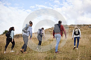 A group of five young adult friends hiking across a field towards the summit, back view