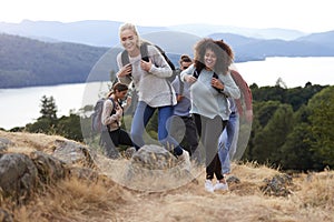 A group of five young adult friends smiling while hiking together to a mountain summit