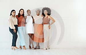 Group of five young happy cheerful businesswomen embracing while standing against a wall in an office. Portrait of