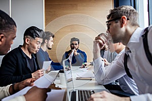 Group focused male business people gathered around computer in office talking.