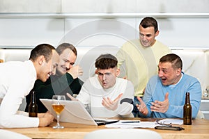 Group of football fans drinking beer and watching football match on laptop at home