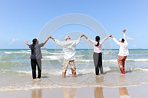 Group of four cheerful elderly old senior friends travel outdoor together, holding and raising hands while running on beach, have