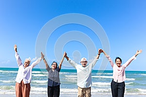 Group of four cheerful elderly old senior friends travel outdoor together, holding and raising hands while standing on beach, have