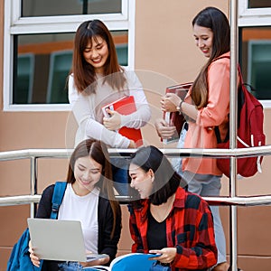 Group of four college student girls holding books and notebook computer sitting and talking together with intimate in front of