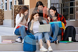 Group of four college student girls holding books and notebook computer sitting and talking together with intimate in front of