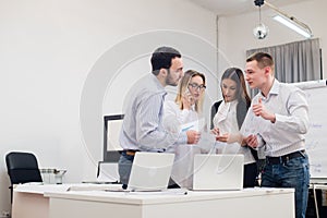 Group of four diverse men and women in casual clothing talking in office