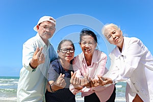 Group of four elderly old senior friends traveling outdoor together, giving mini heart to camera, have fun and enjoy spending time