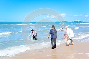 Group of four elderly old senior friends traveling outdoor together, playing in shallow sea water, have fun and enjoy spending