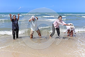 Group of four elderly old senior friends traveling outdoor together, playing in shallow sea water, have fun and enjoy spending