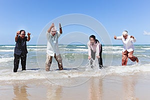 Group of four elderly old senior friends traveling outdoor together, playing in shallow sea water, have fun and enjoy spending