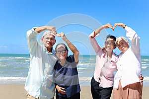 Group of four elderly old senior friends traveling outdoor together, posting to camera, have fun and enjoy spending time on sand