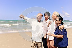 Group of four elderly old senior friends traveling outdoor together, take a selfie on mobile phone, have fun and enjoy spending